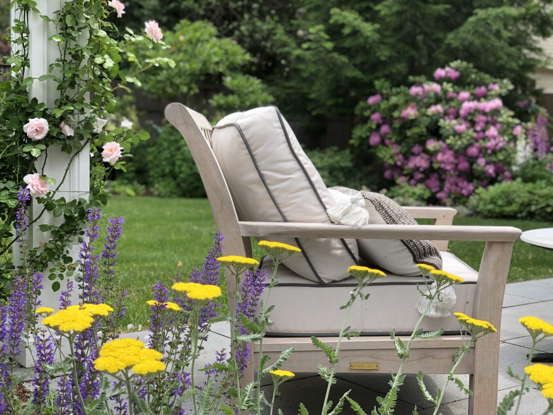 A serene garden with a comfortable wooden chair surrounded by vibrant flowers, including pink roses and yellow blooms, invoking a sense of tranquility.