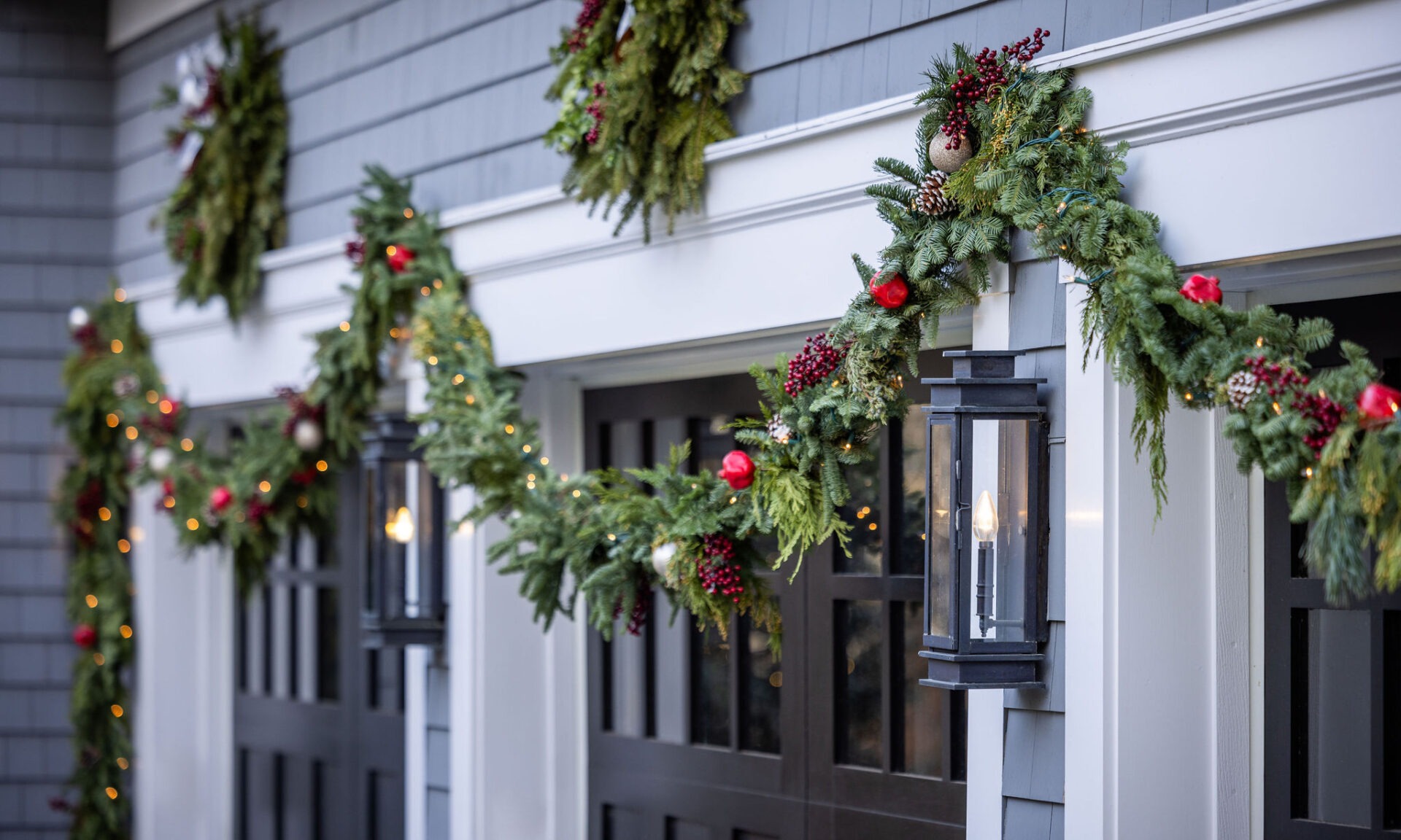 An outdoor holiday decoration with evergreen garlands, red ornaments, and lights adorning a building's exterior, featuring a lantern and festive ambiance.