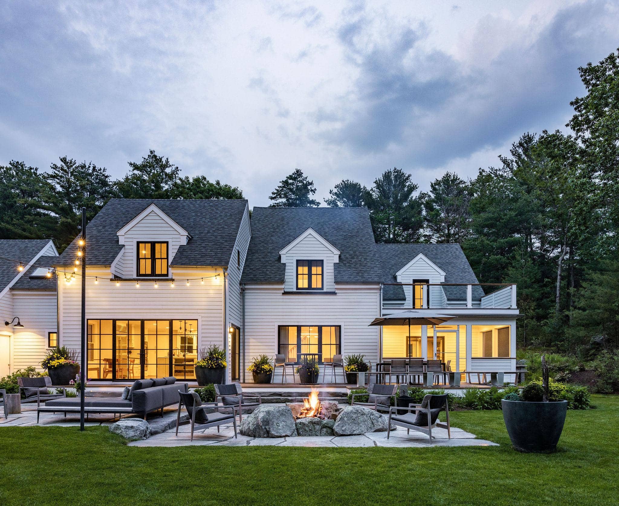 High-end residential home with landscaped patio, fire pit, and outdoor seating surrounded by mature trees at dusk