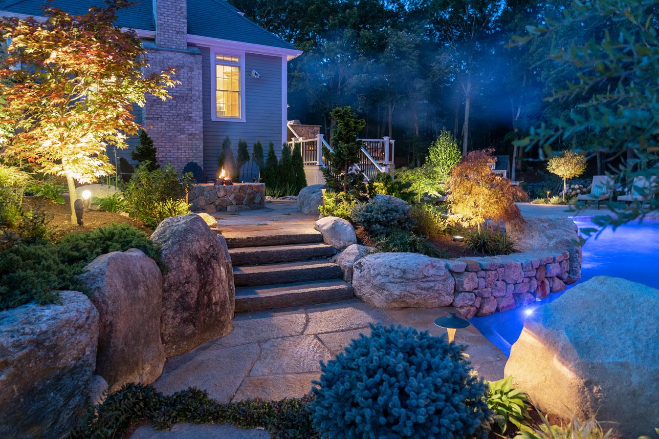 Residential landscape with stone steps, accent lighting, and natural boulders at dusk